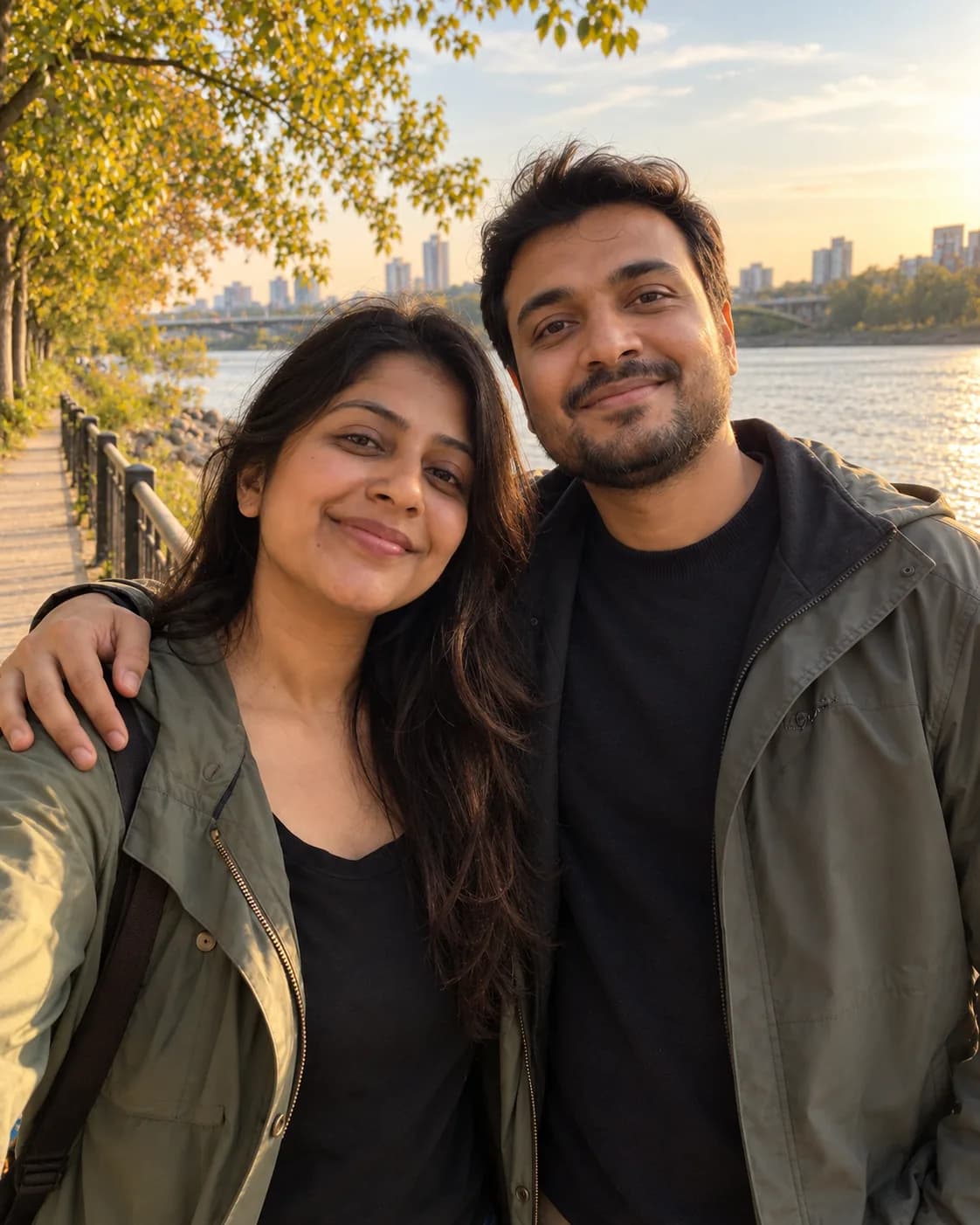 Couple on a riverside promenade at golden hour, his arm around her shoulder.
