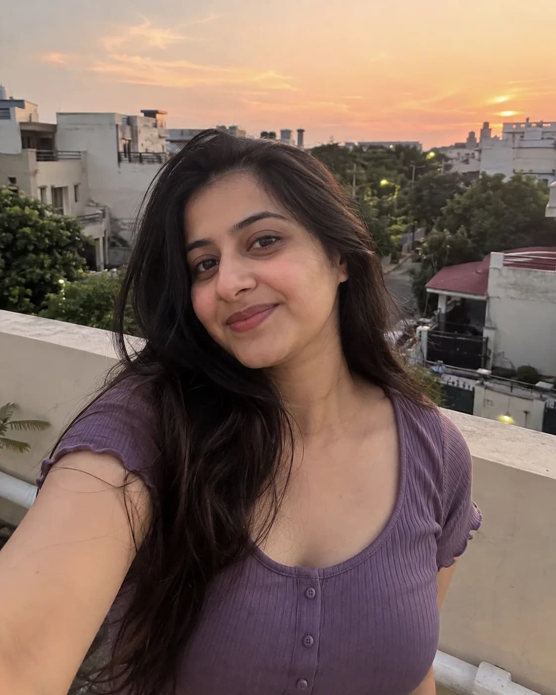 Woman in a purple top, rooftop selfie at sunset.