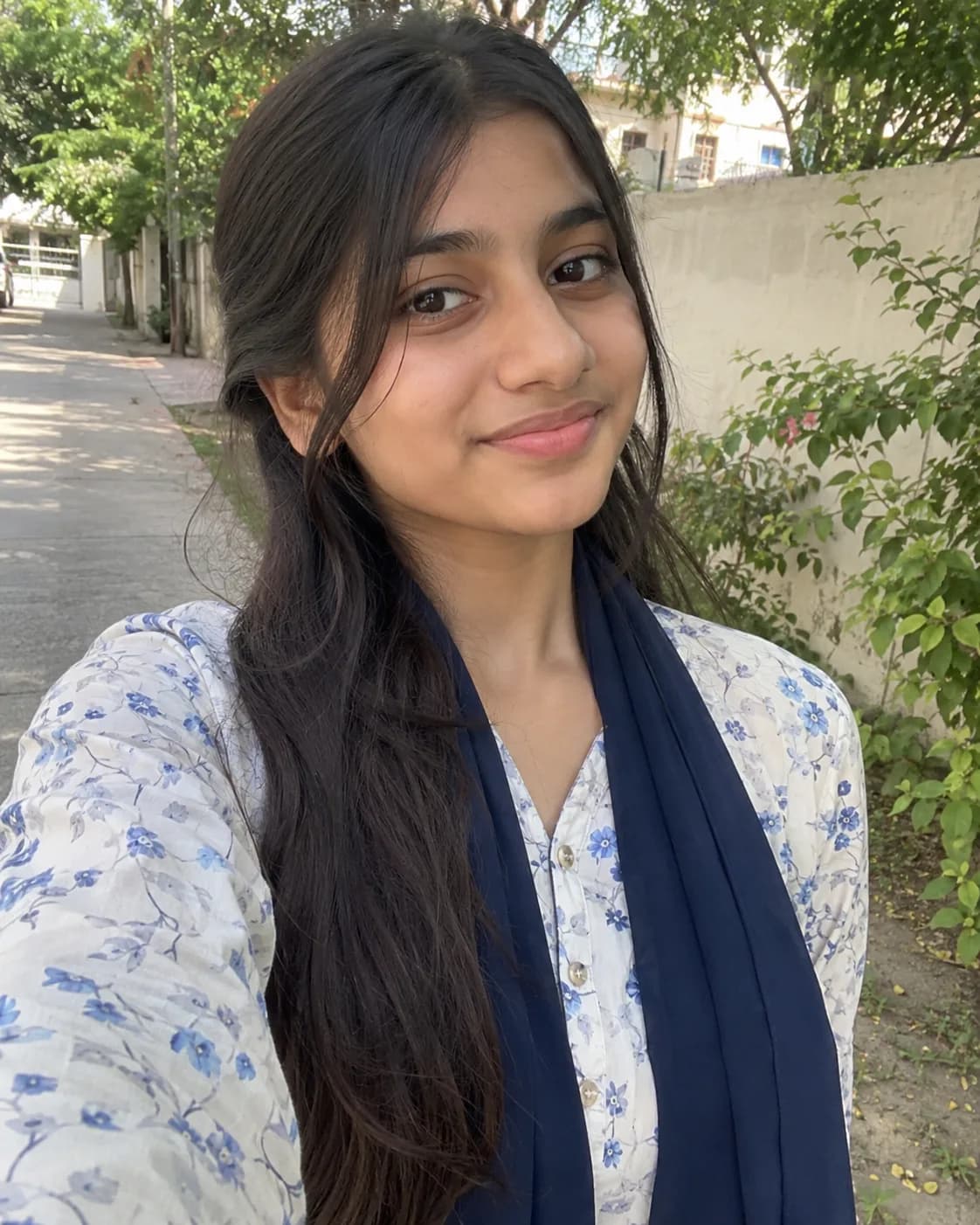 Teen girl in a white and blue floral kurti and navy dupatta, on a garden path.