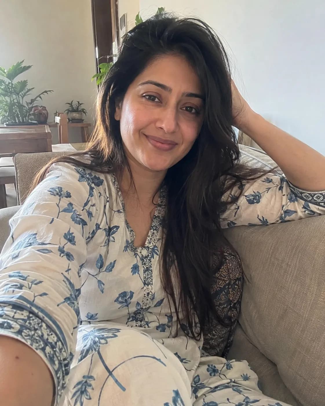 Woman in a white and blue floral kurti on a beige sofa.