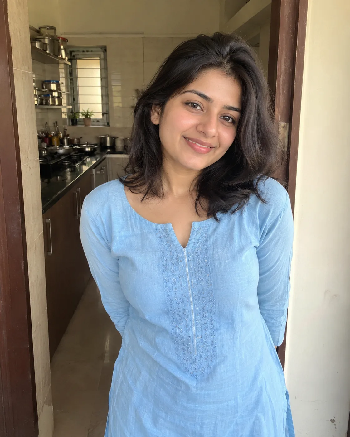 Woman in a light-blue embroidered kurta in a kitchen doorway.